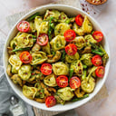Foto de Tortellini de espinaca y ricota, con tomates cherry salteados, salsa bechamel y chips de albahaca.