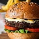Foto de CLÁSICA: hamburguesa artesanal de carne, acompañada de crujientes papas nativas, lechuga y tomate