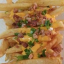 Foto de Porción de papas fritas con queso cheddar, panceta asada y cebolla de verdeo