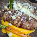 Foto de Solomillo de cerdo ibérico envuelto en guanciale, con cremoso de calabaza asada al carbón, migas al ajillo y queso de oveja